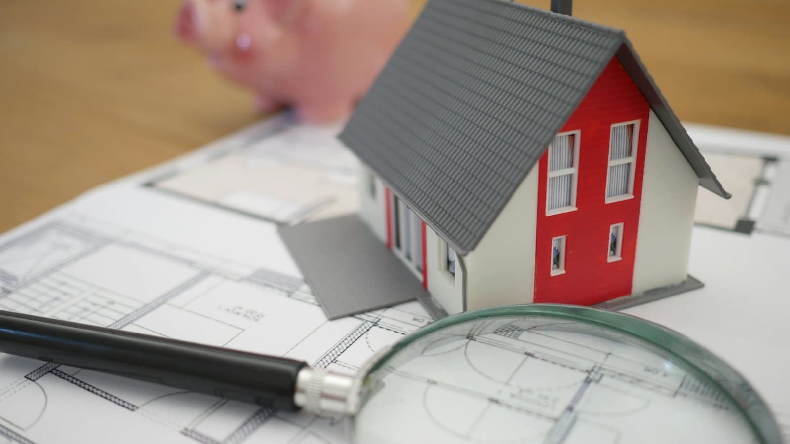 Model house, magnifying glass and piggy bank on a set of floor plans