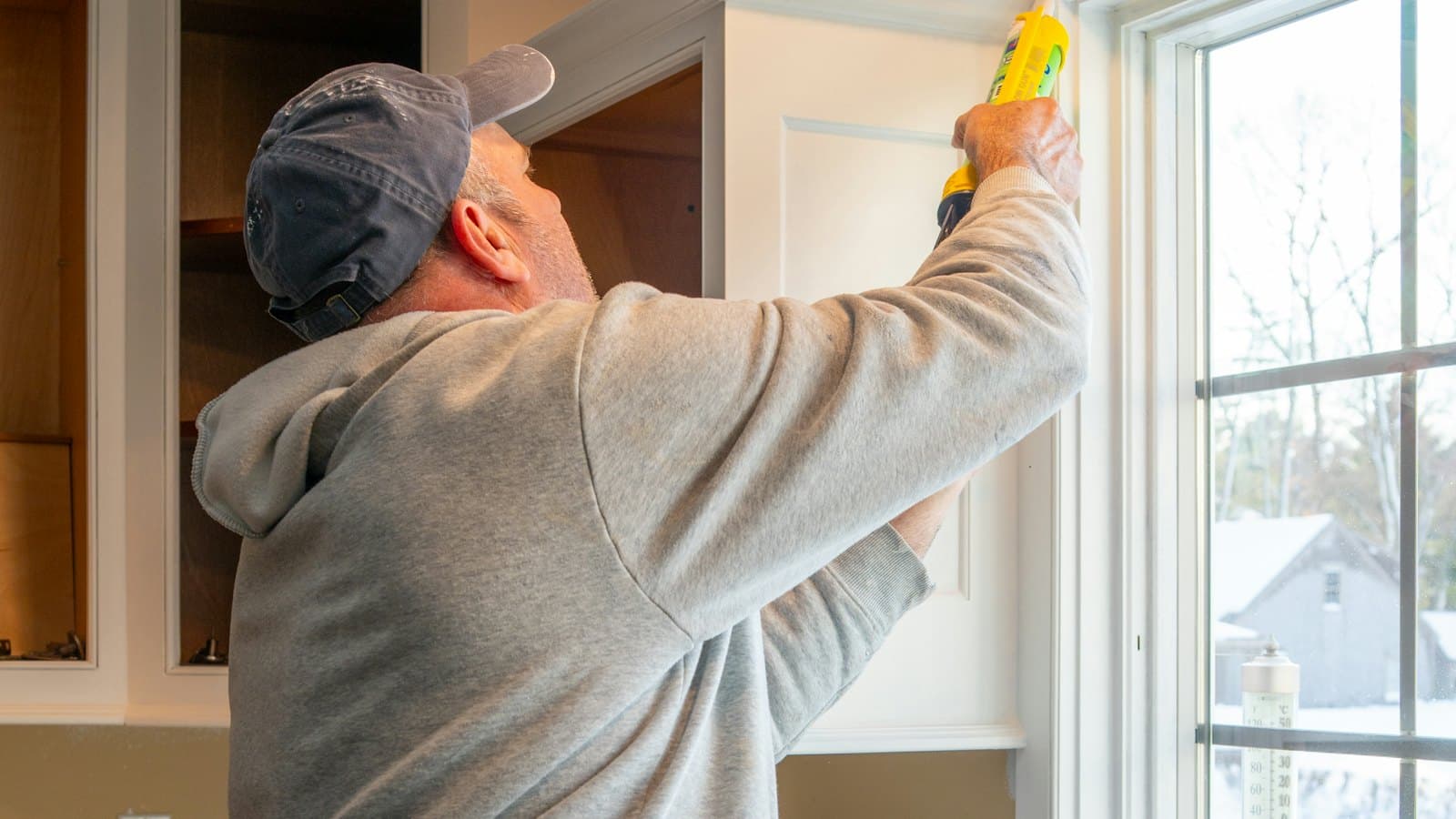 Homeowner applying caulk around a window frame