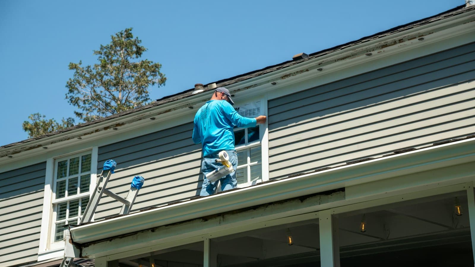 Worker on a porch roof servicing the upstairs windows of a house