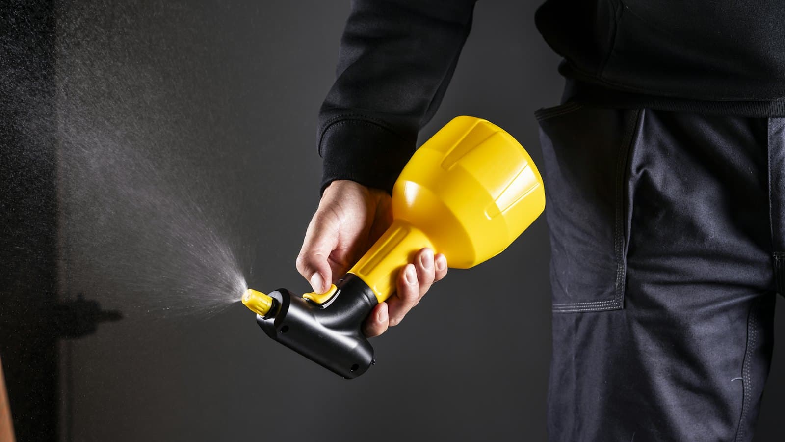 Hand holding a yellow pressure sprayer misting a treatment